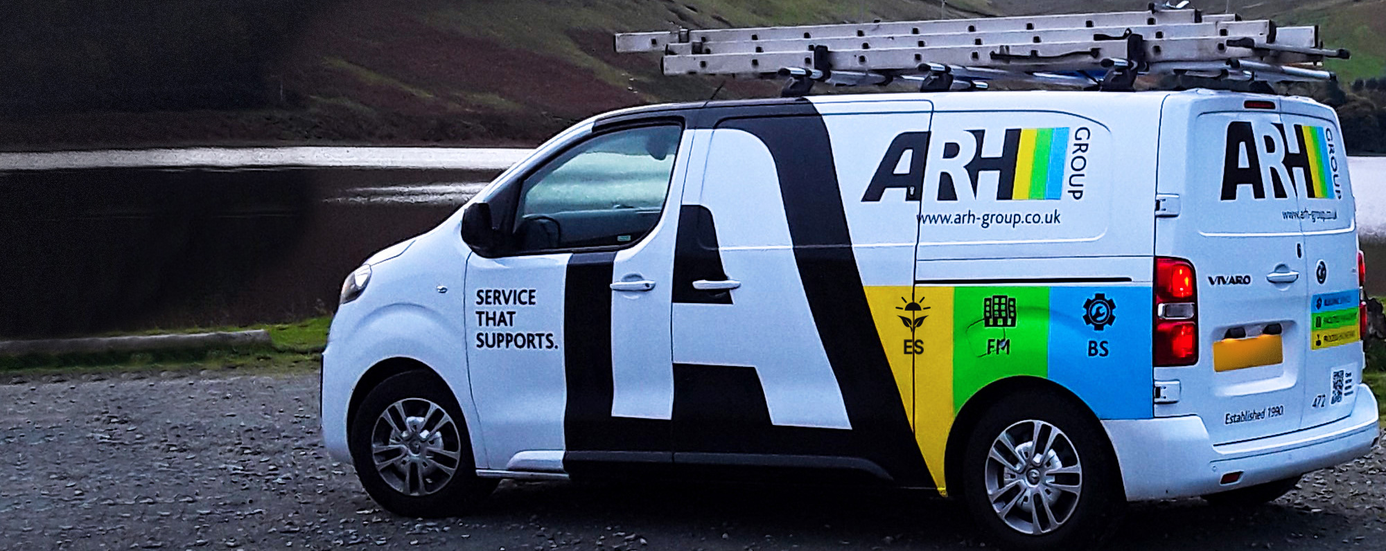 An ARH Group van stands ready by a peaceful lakeside, fully equipped for electrical, building, and facilities services—where support meets scenery.