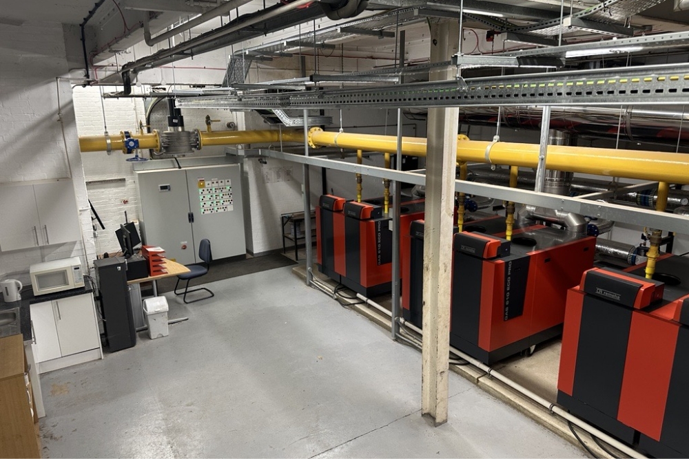 An organized boiler room featuring red and black heating units, overhead yellow piping, and a compact workspace—designed for efficient industrial operations.