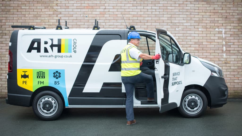 Wearing full safety gear, a technician enters an ARH Group van marked with the company’s branding and service categories—PE, FM, and BS—ready to deliver reliable support.