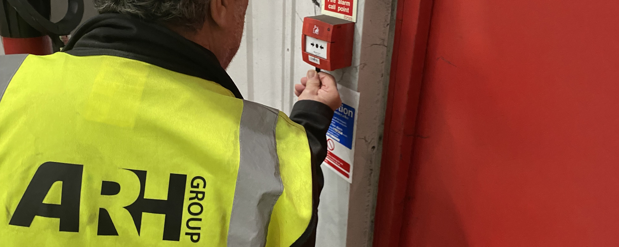 An ARH Group technician conducts a routine test on a fire alarm call point, ensuring safety systems are fully operational.